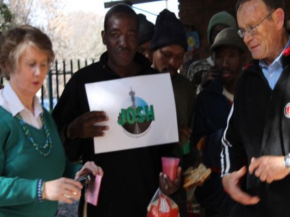 Mary Gillett-de Klerk  presents the voucher to Arthur Mbeye from Malawi (with the Josh poster), while Mike Wood the Ward 104, who bought the first voucher councillor looks on, during the launch of the voucher scheme at the  on the Mandela Day.